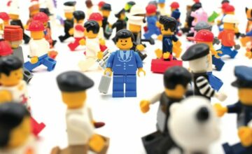 A crowd of LEGO minifigures walking in all directions, one stands in the middle facing the camera