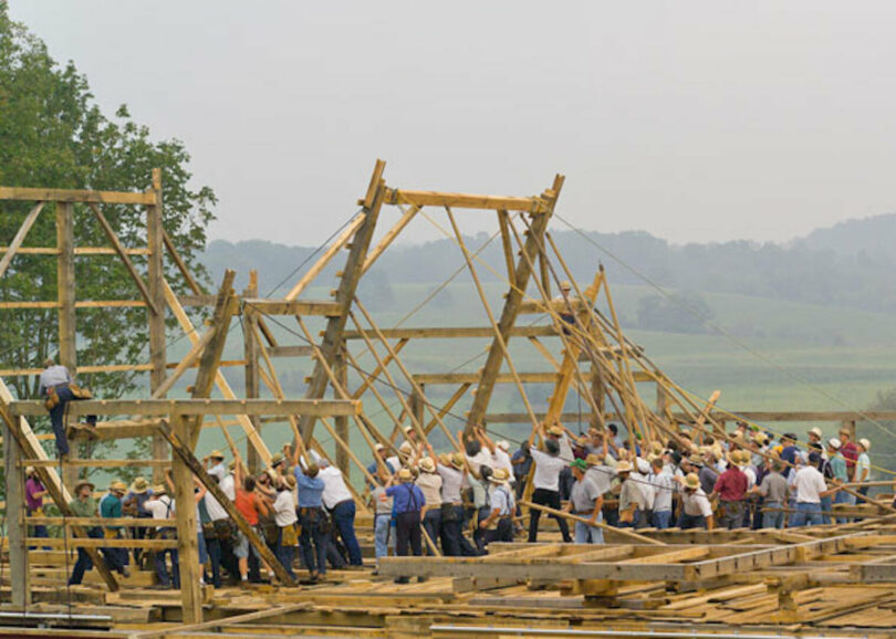 Photo of a large group of community members working together to build or rebuild a barn